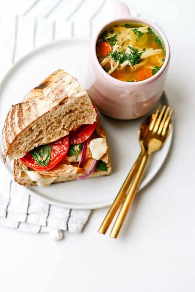 a quarter of a smoked chicken sandwich with a cup of chicken soup on the side.